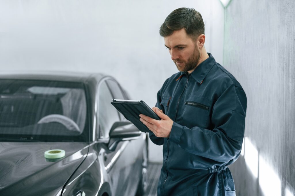 Reading information. Car painter is standing in the garage with documents in hands